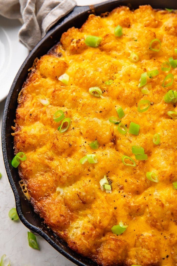 Cast iron skillet holding a tater tot breakfast casserole with cheese, sausage, and eggs, topped with chives