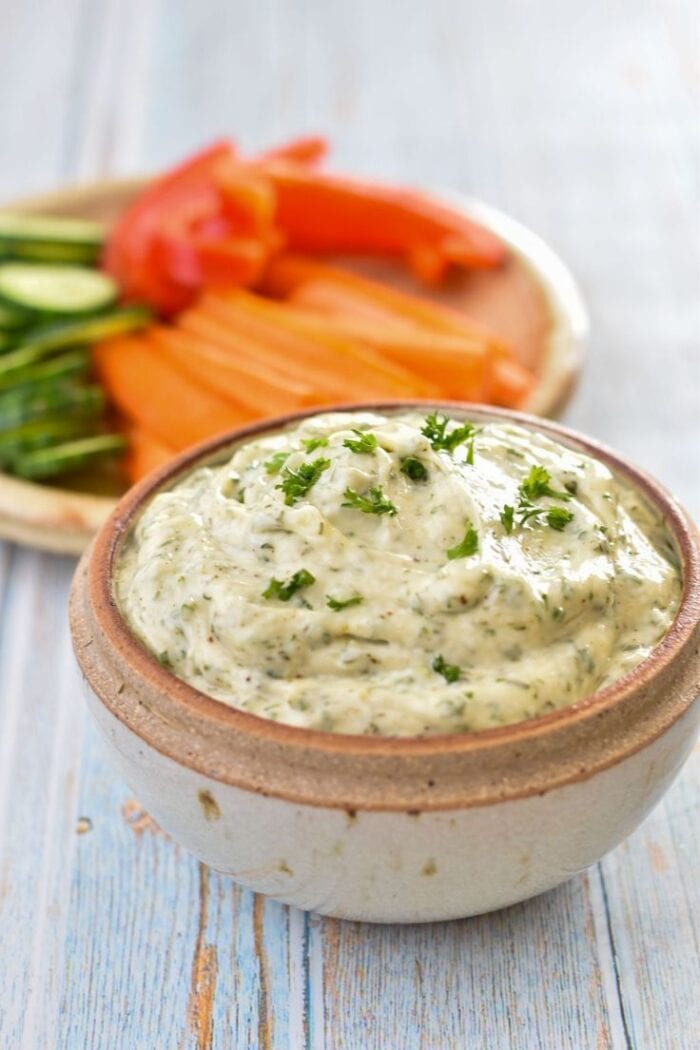 Whole30 dill veggie dip in a neutral bowl in front of a plate of veggies