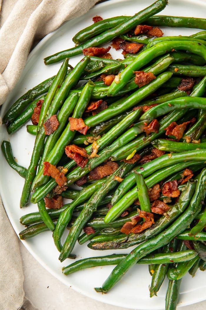 White plate holding sauteed green beans and bacon