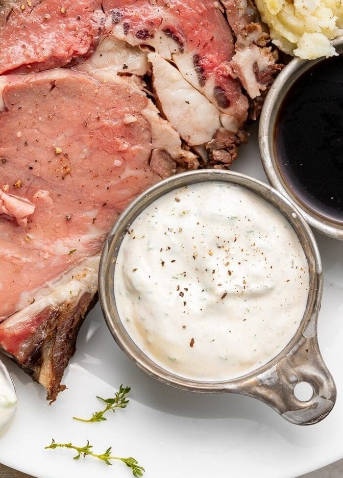 A side of horseradish sauce next to prime rib on a white plate
