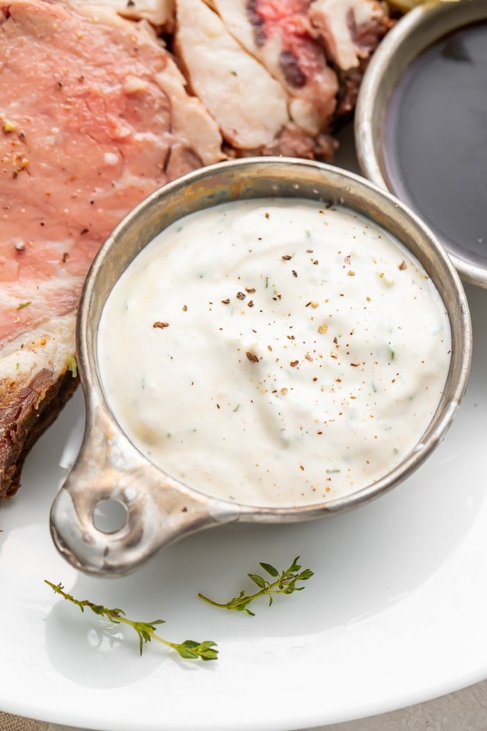 Close up of a silver dish with horseradish sauce next to prime rib on a plate