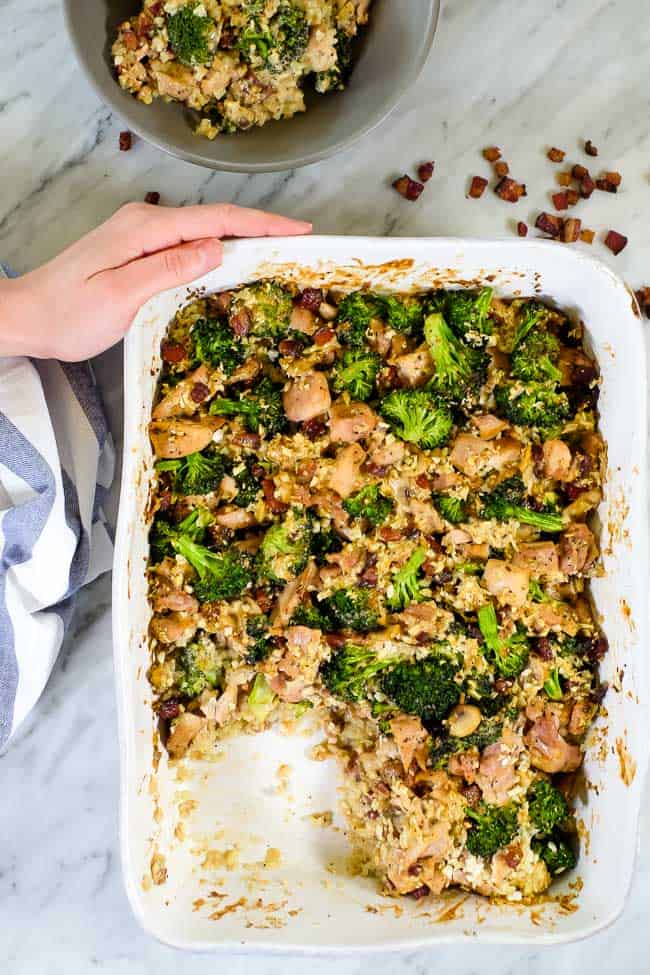 A baking dish full of broccoli and chicken casserole with one scoop missing