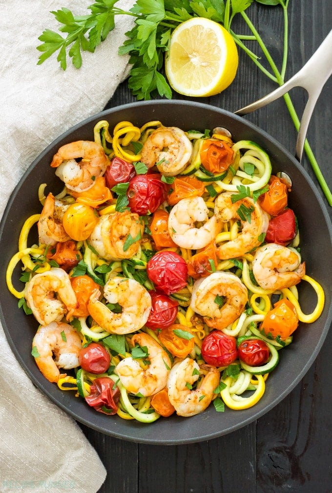 Cast iron skillet with zucchini zoodles, shrimp, and roasted tomatoes, garnished with lemon
