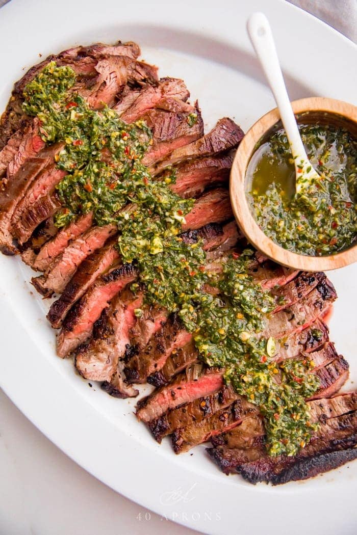 Paleo flank steak topped with chimichurri on a white serving platter