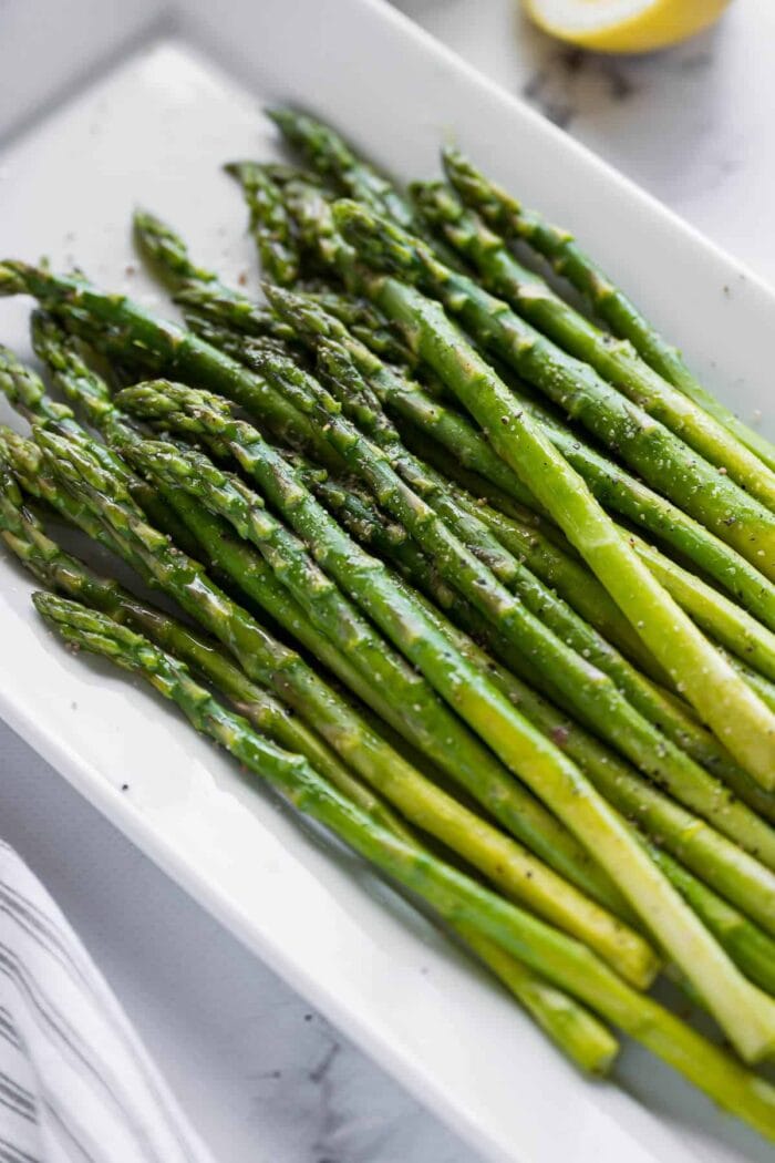 A white platter holding cooked asparagus stalks