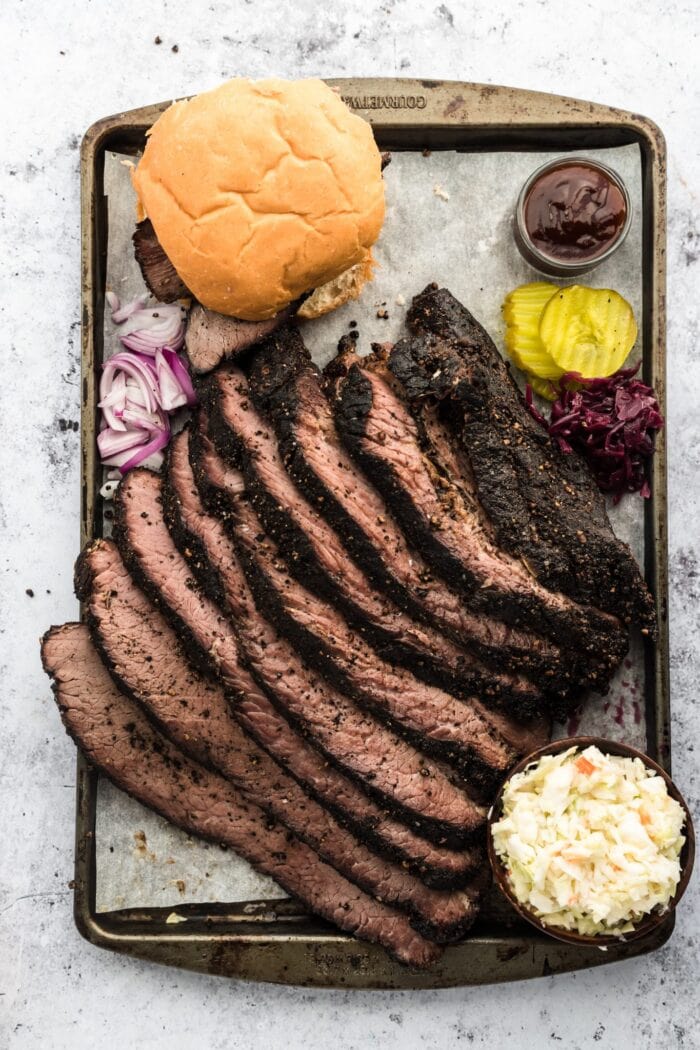 Sliced brisket on a sheet pan with bread and garnish