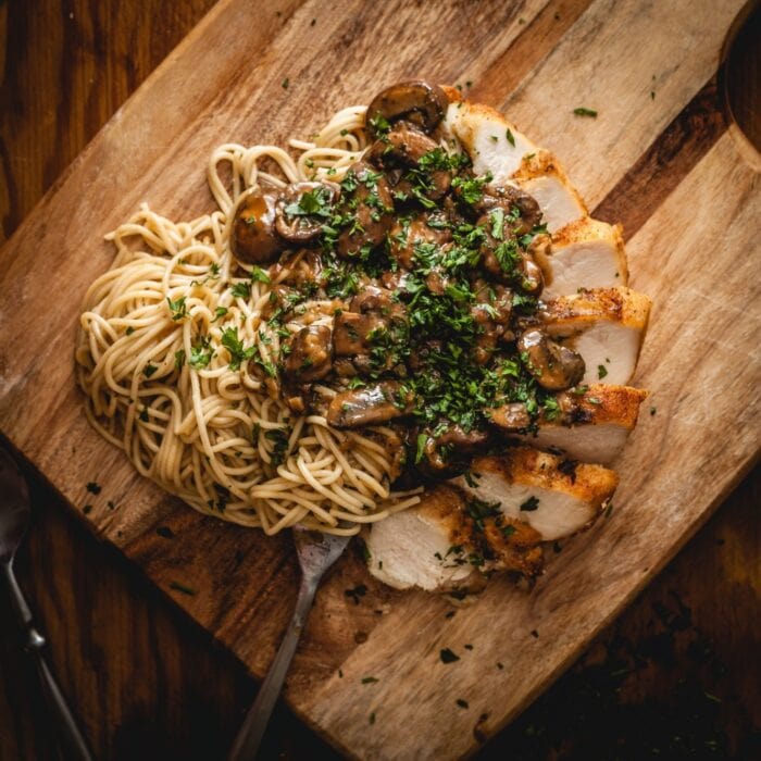 Closeup of pasta, chicken marsala, and mushrooms on a cutting board
