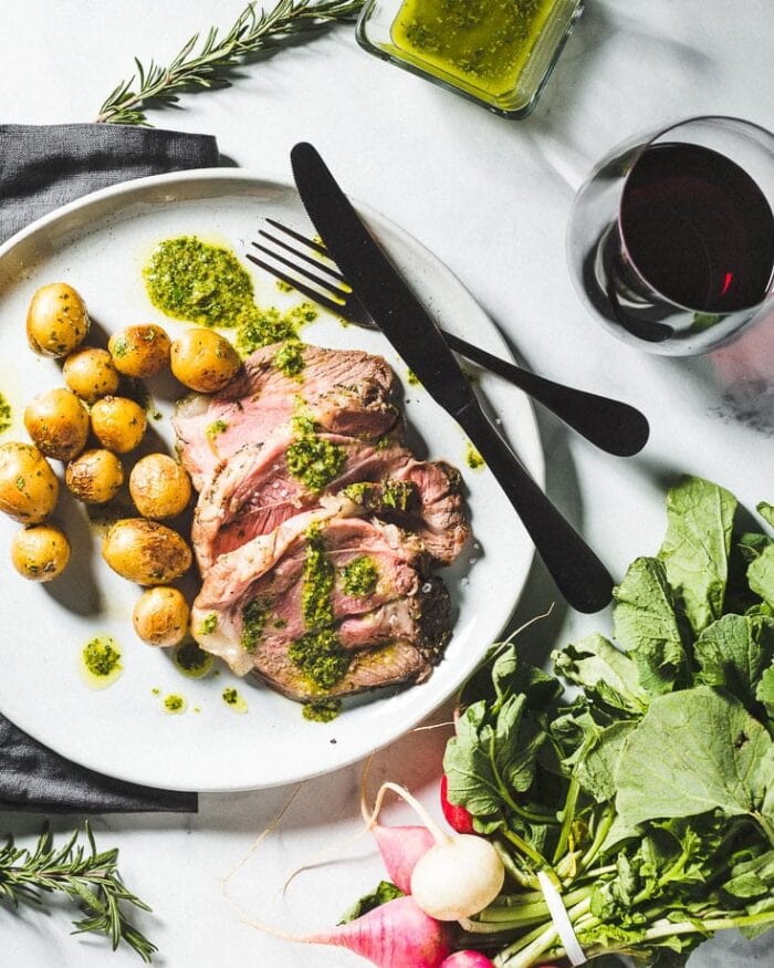Plated leg of lamb with potatoes, lettuce, and black silverware