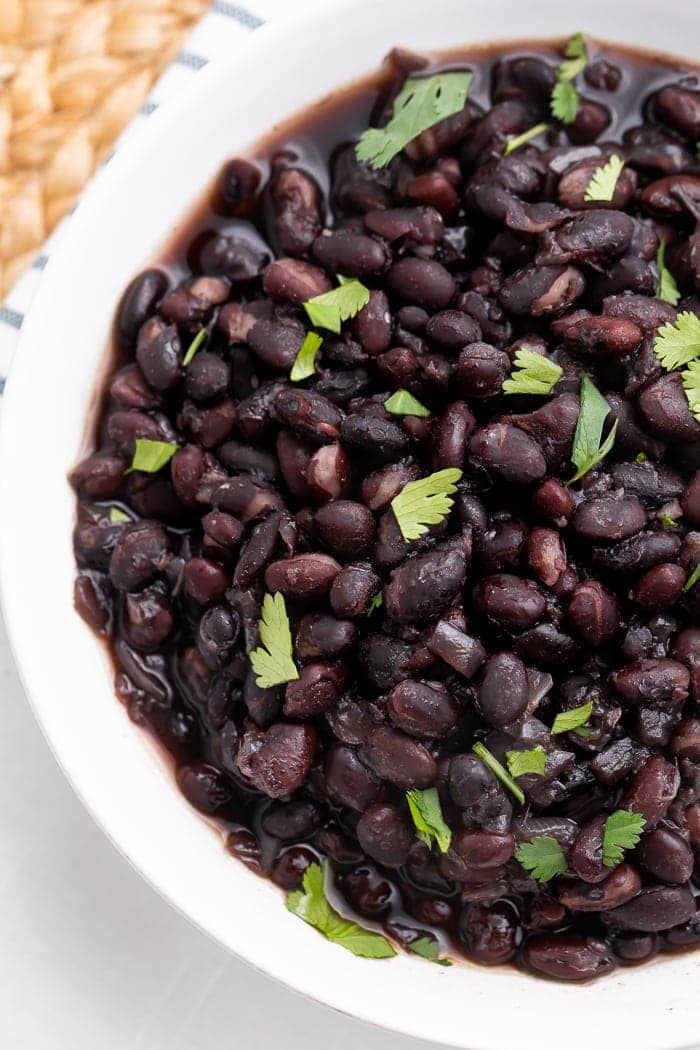 Overhead view of a partial view of a white bowl holding Instant Pot cooked black beans with garnish