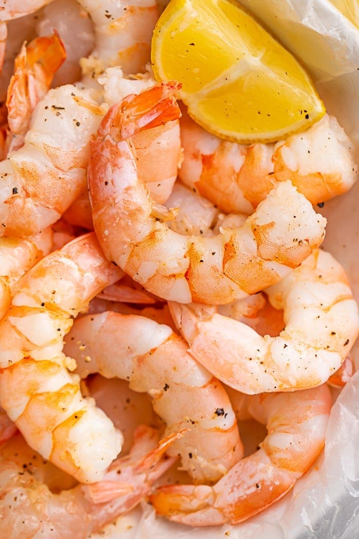 Closeup of cooked shrimp in a bowl with a lemon wedge