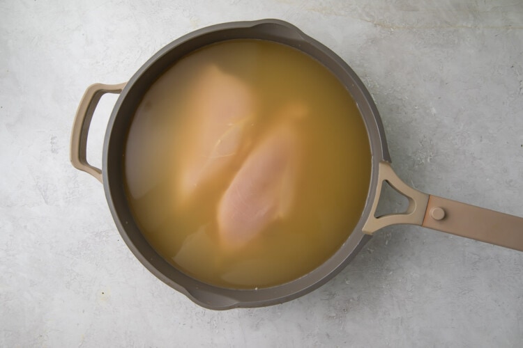 Chicken breasts covered with chicken stock in a large skillet
