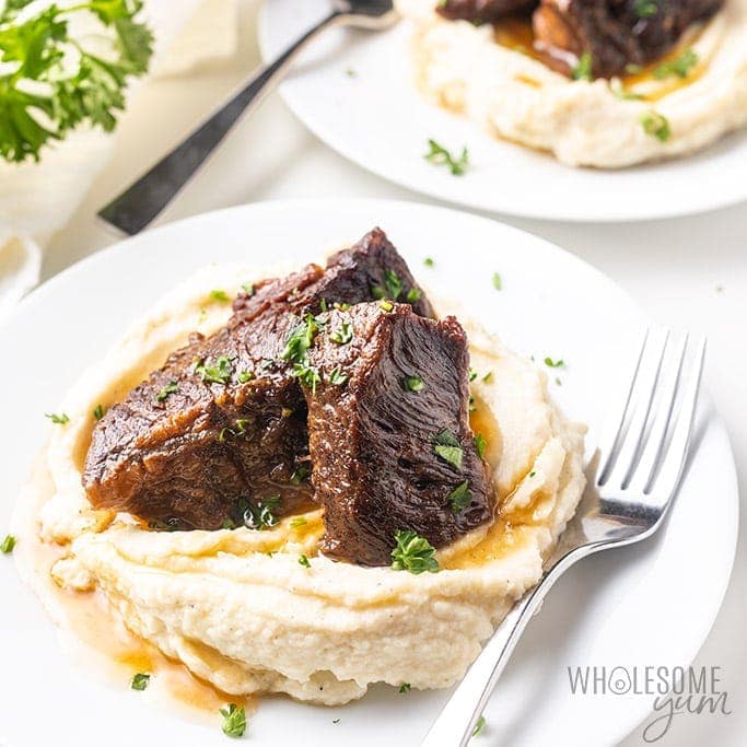 Beef short ribs on top of mashed potatoes on a white plate