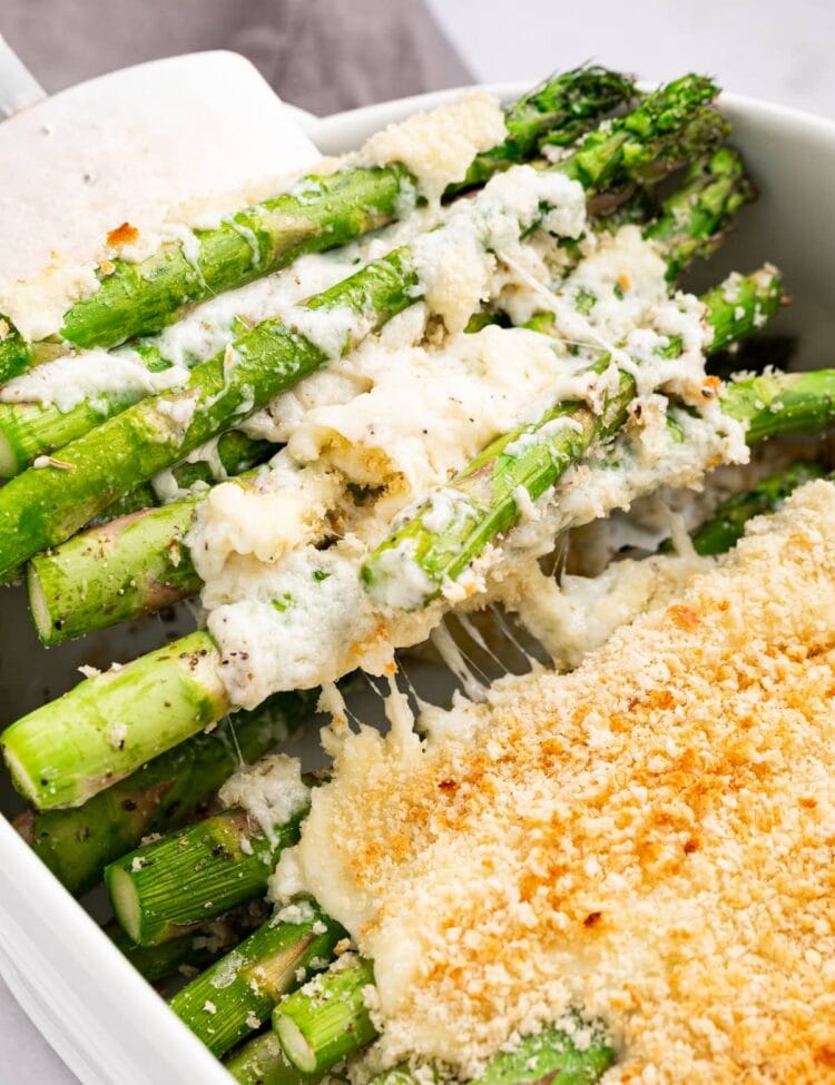 Asparagus casserole being scooped out of the baking dish with a spatula.