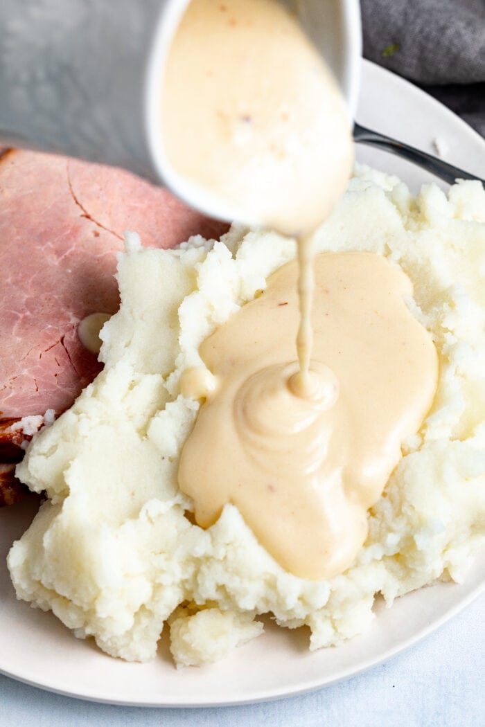 Ham gravy poured over mashed potatoes with sliced ham on the side.