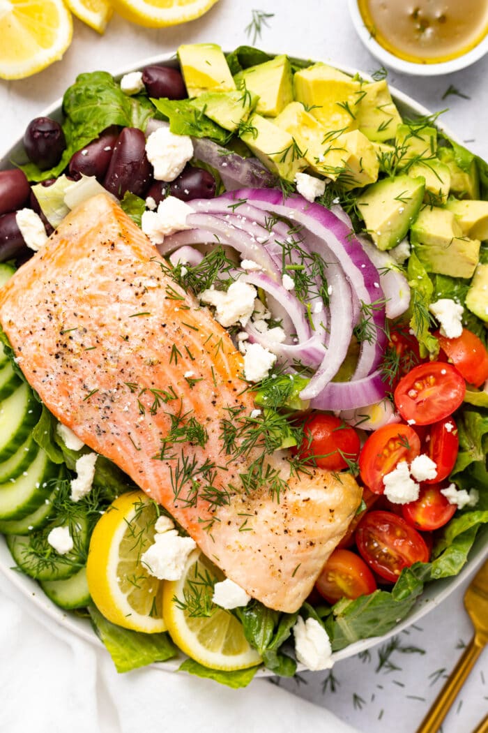Salmon filet over salad with lemon and dressing on the side.