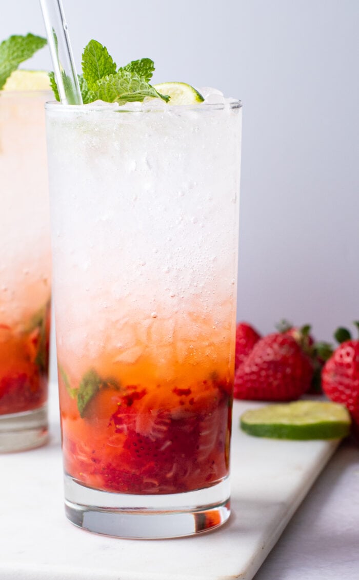 Strawberry mojito in a tall glass with ice topped with mint leaves