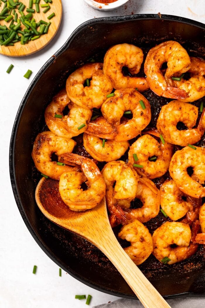 Cajun shrimp in a skillet with chives on the side.