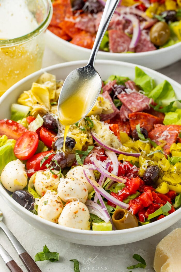 Italian vinaigrette spooned over an antipasto salad in a large bowl.
