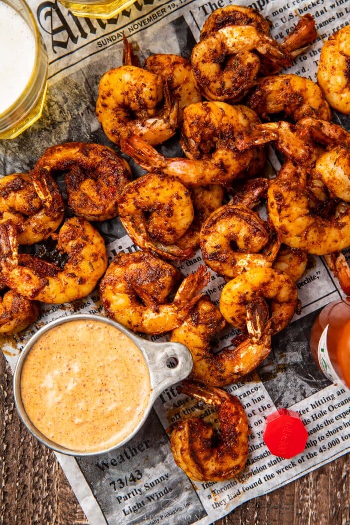 A pile of blackened shrimp on newspaper next to a dipping cup of remoulade sauce