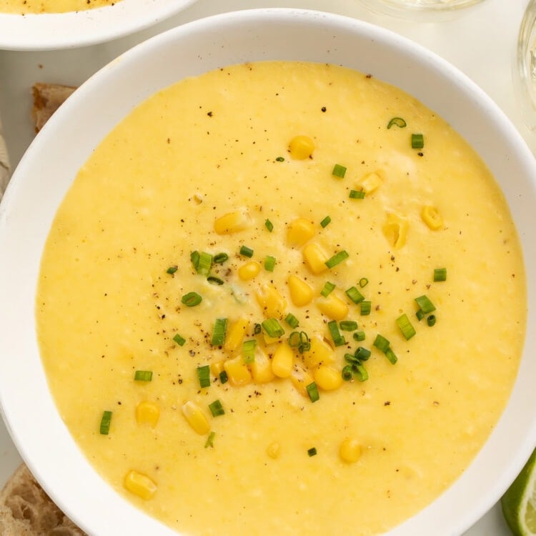 A white soup bowl holding a thick, creamy yellow corn soup topped with corn kernels and chopped green onions.