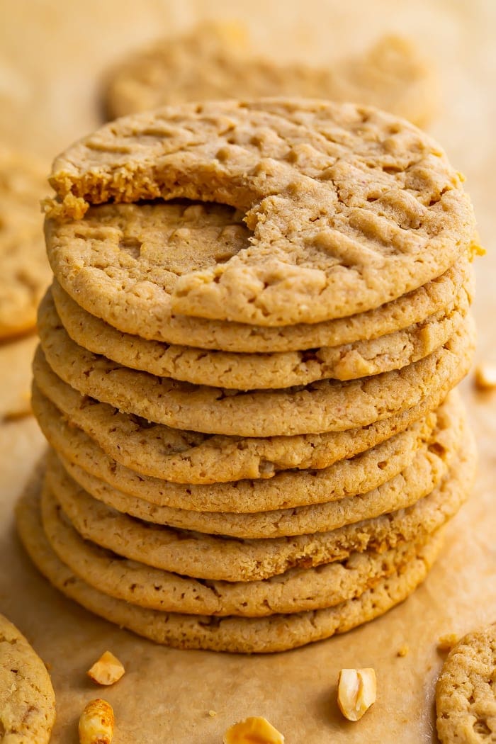 Stack of round gluten free peanut butter cookies on parchment paper. Top cookie has one bite missing.