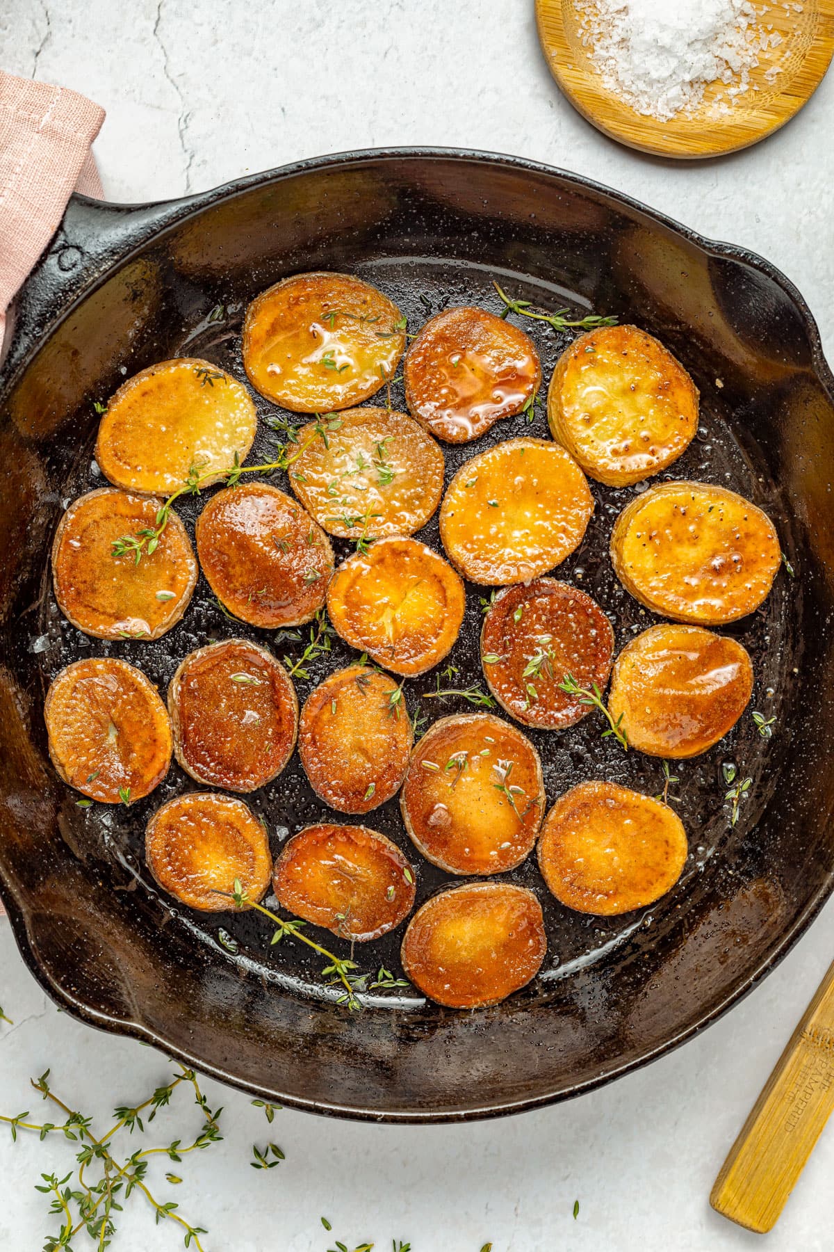 Top-down view of pan fried potatoes in a single layer in a large black cast iron skillet on a marble countertop.