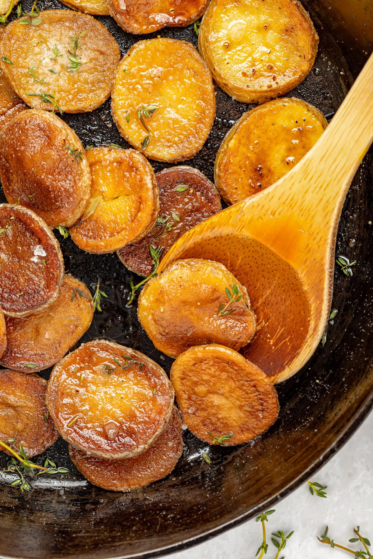 Crispy, pan fried potatoes in a black cast-iron skillet with a wooden spoon.