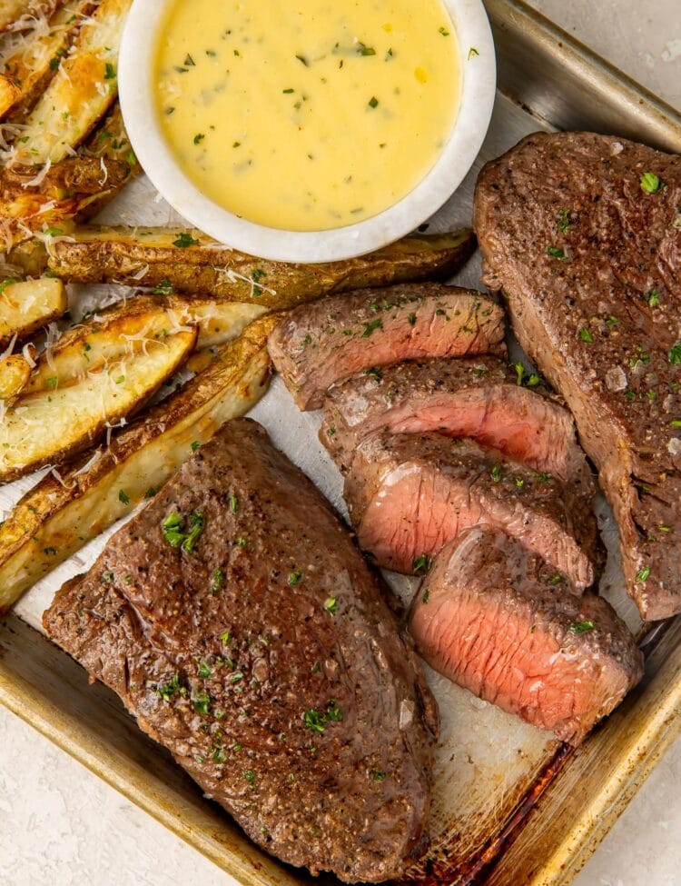 Medium rare steak and thick cut fries with a bowl of bearnaise sauce on a sheet pan