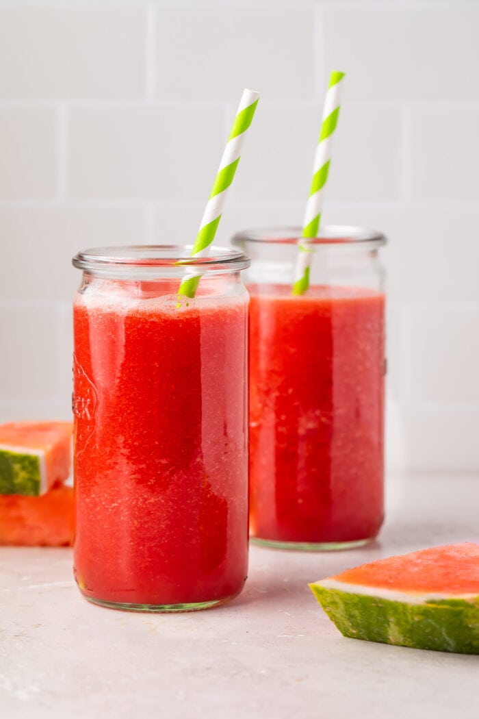 Two glasses of watermelon juice with green and white striped straws