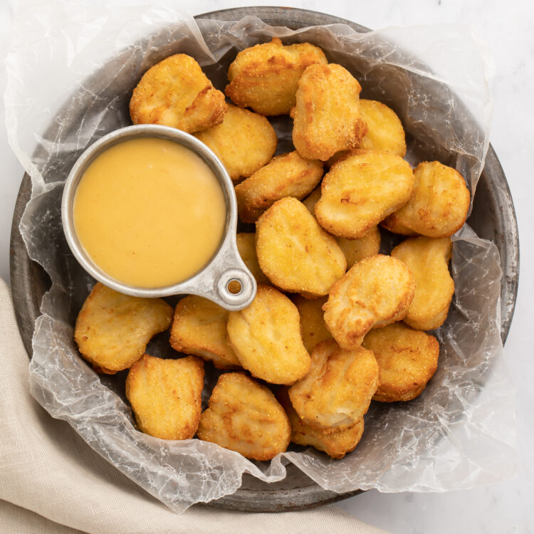 Overhead view of a large bowl of air fryer frozen chicken nuggets with a small dipping bowl of honey mustard.