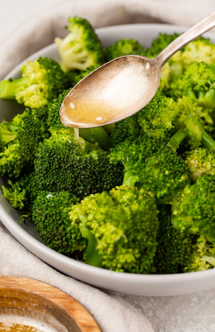 A spoon drizzles lemon butter sauce over Instant Pot broccoli in a large white bowl