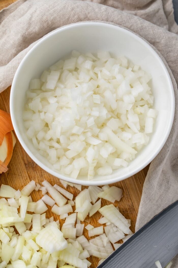 Diced onion on a cutting board next to a bowl of diced onion