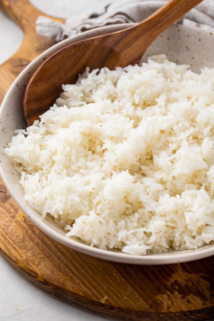 Angled photo of Instant Pot jasmine rice with a wooden spoon in a large bowl on a wooden tray with a cloth napkin
