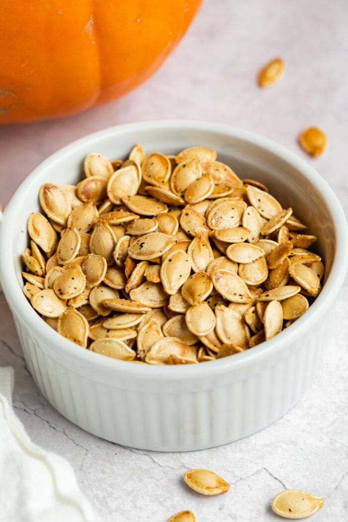 air fryer pumpkin seeds in a dish with a pumpkin on the side