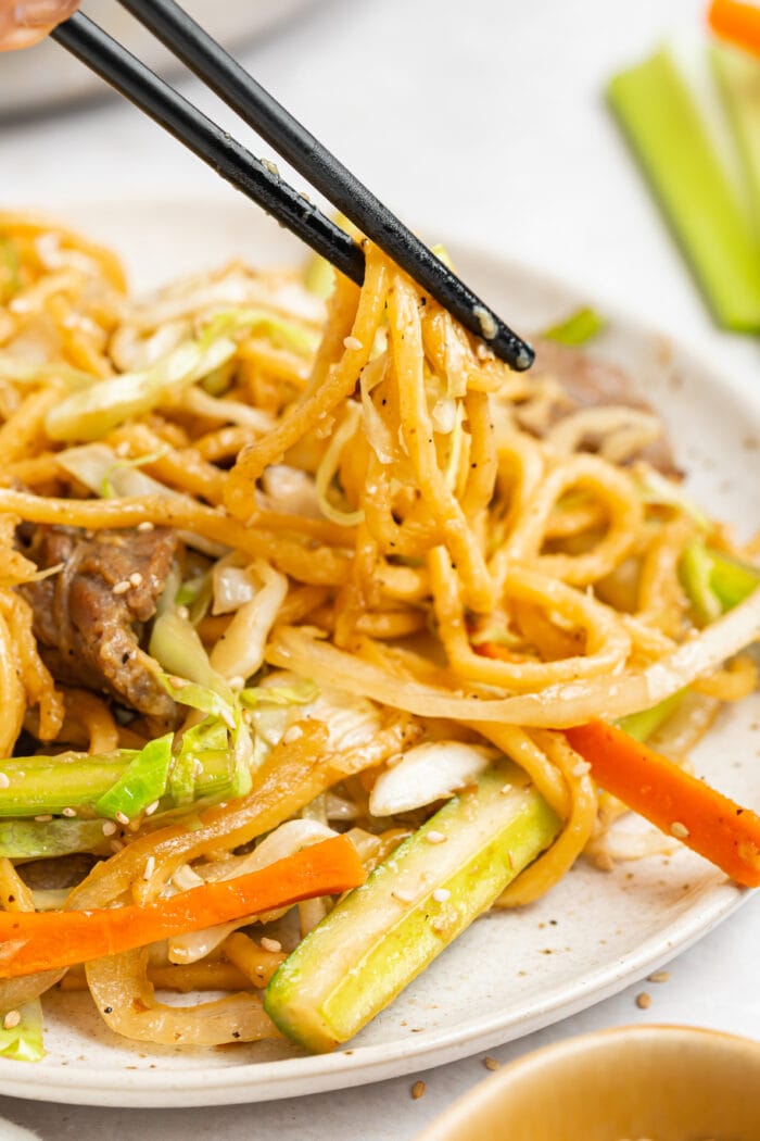 beef chow mein being lifted off a plate with chopsticks