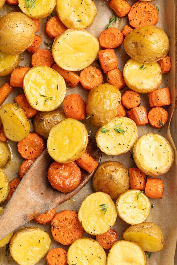 roasted potatoes and carrots on a baking sheet with fresh thyme on top and a wooden spoon