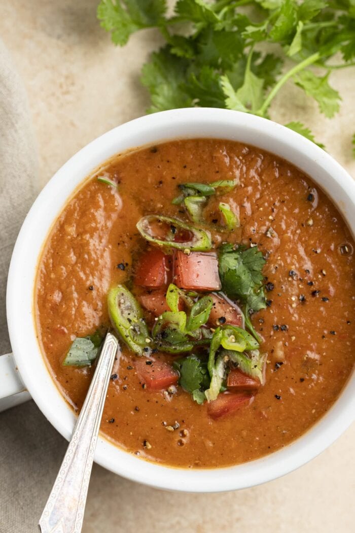 A large cup of pinto bean soup topped with cilantro, lime, tomatoes, and green onions