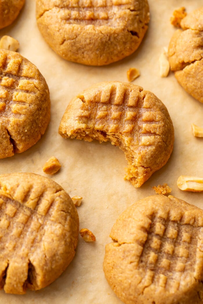 3 Ingredient Peanut Butter Cookies on a parchment paper lined baking sheet, with one bite taken out of the center cookie