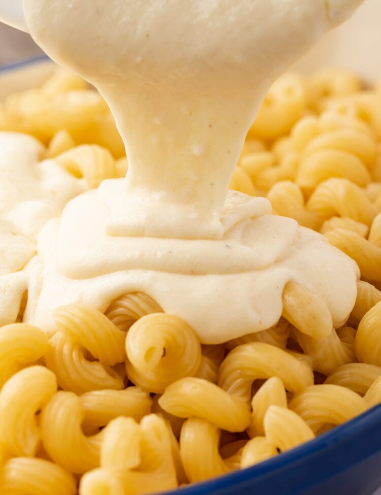 Mornay sauce being poured over a bowl of spiral noodles