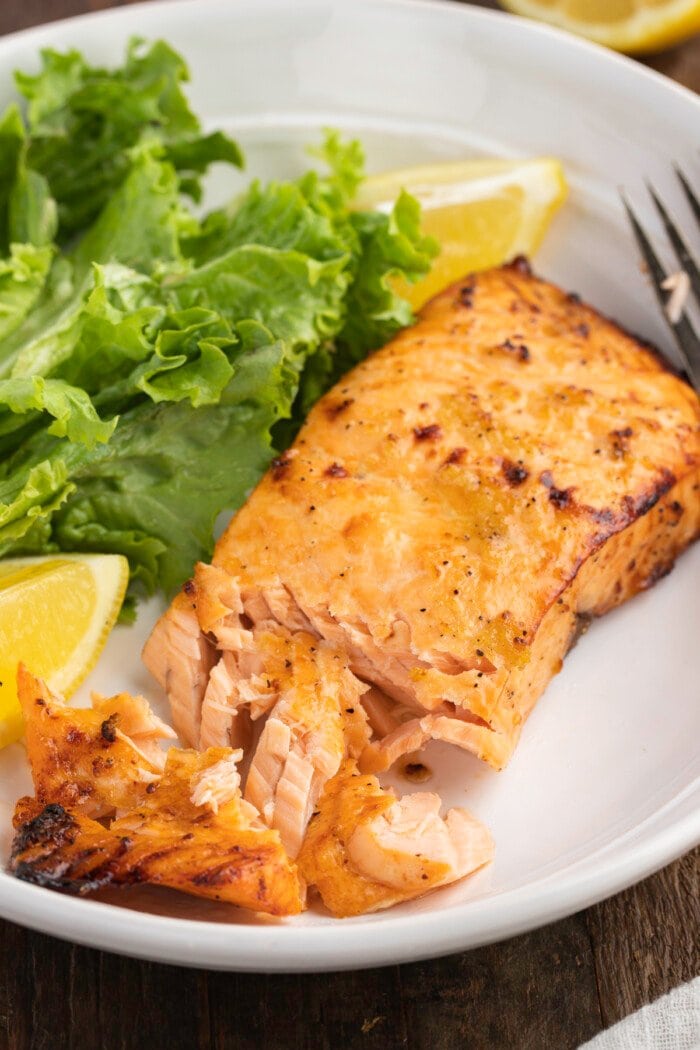 3/4-angle view of flaky air fryer salmon fillet on a plate with a small green salad and lemon wedges.