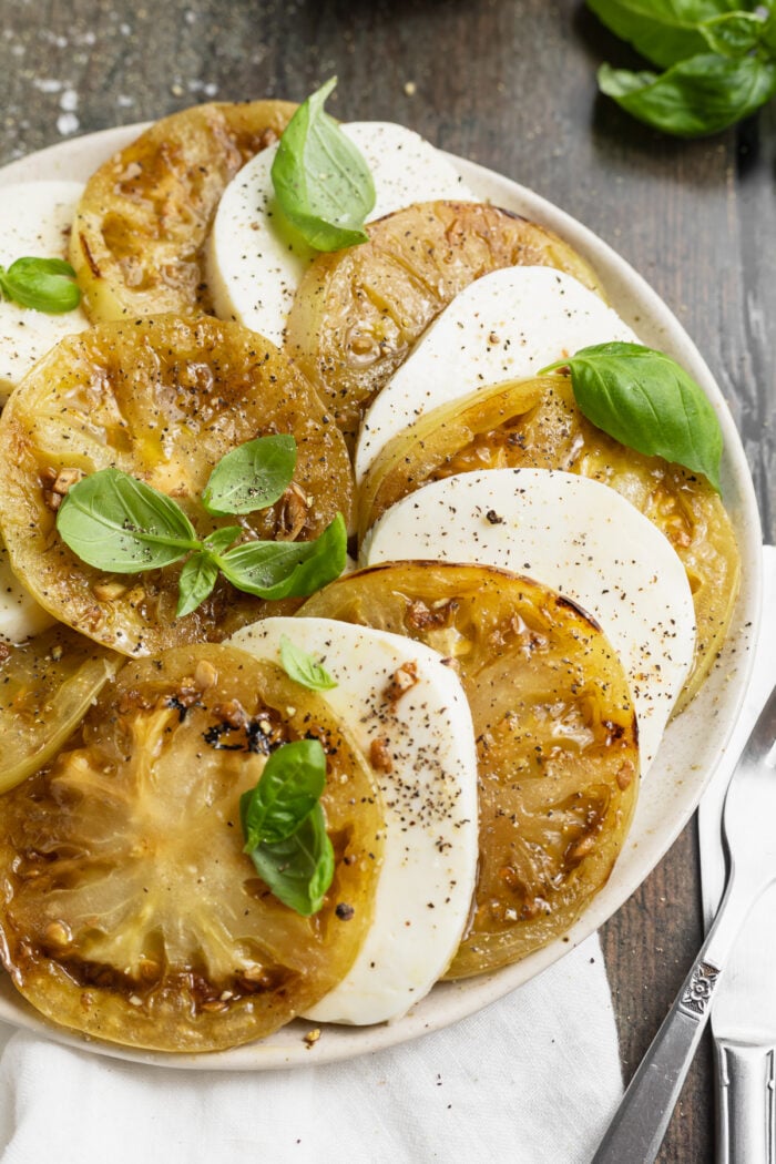 Overhead view of slices of grilled green tomatoes and fresh mozzarella arranged in a circle on plate.
