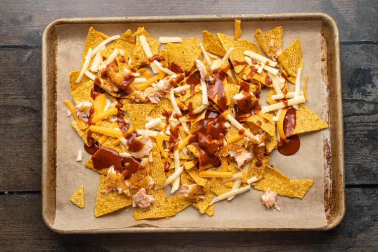 Baking sheet topped with tortilla chips, cheese, and BBQ sauce.