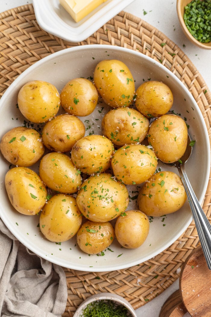 Overhead, zoomed out view of a bowl of boiled baby potatoes with rosemary and garlic in a bowl.