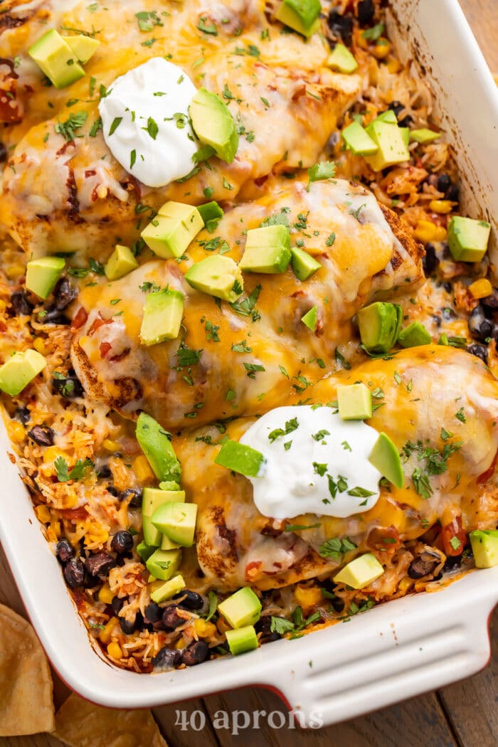 Overhead, angled view of a Mexican chicken and rice casserole with corn, black beans, sour cream, and diced avocado.