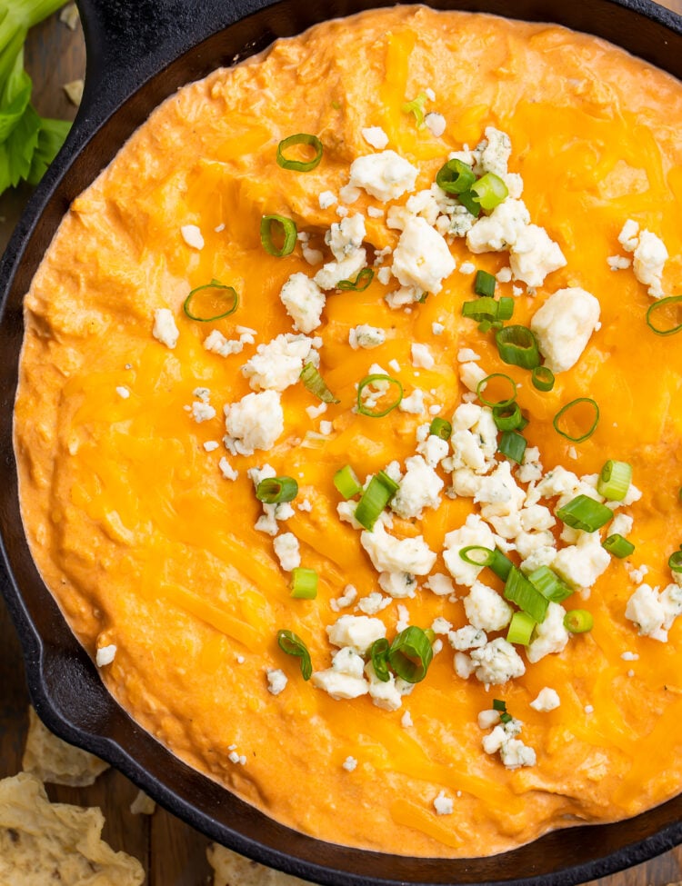 Overhead view of Instant Pot buffalo chicken dip in a cast-iron skillet. Dip is topped with blue cheese crumbles and green onions.