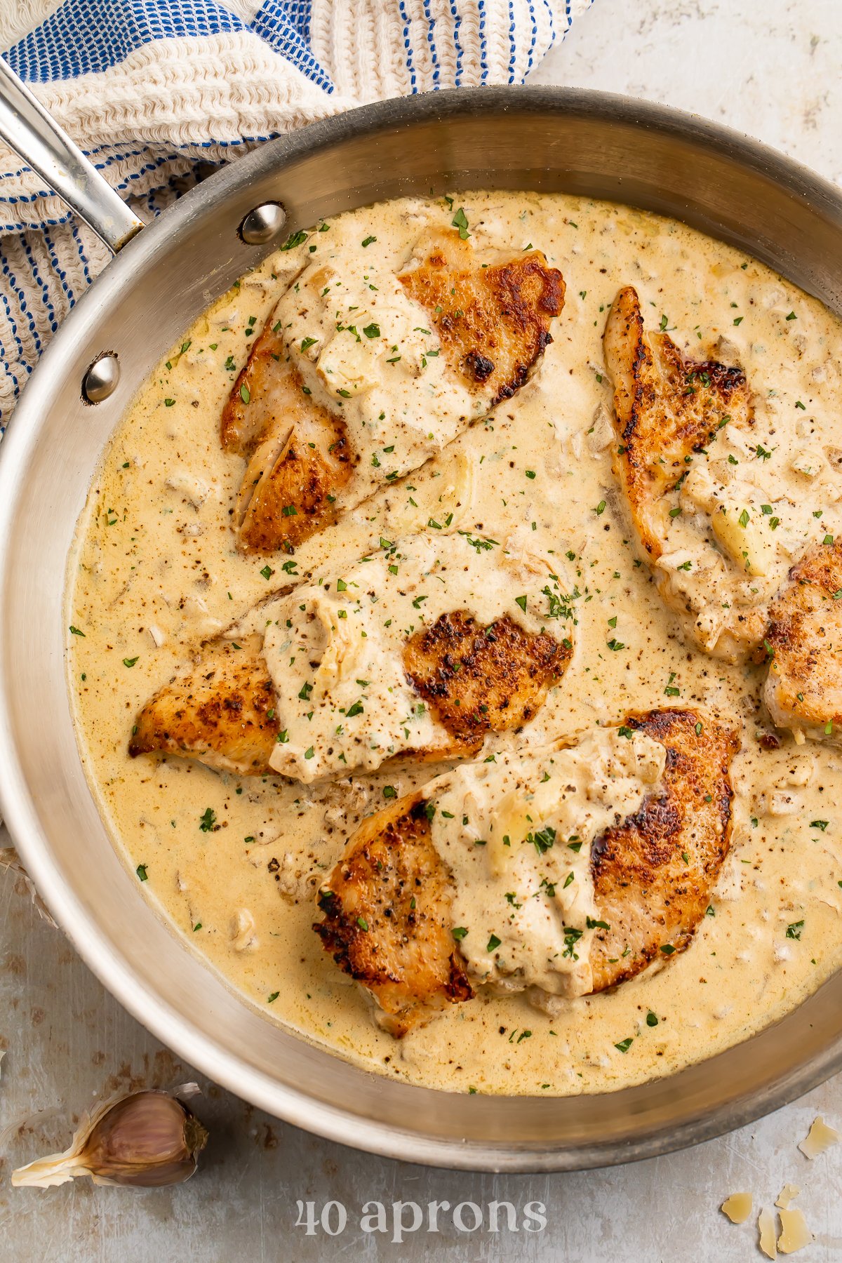 Overhead view of 4 chicken breasts in a creamy garlic sauce in a large silver skillet.