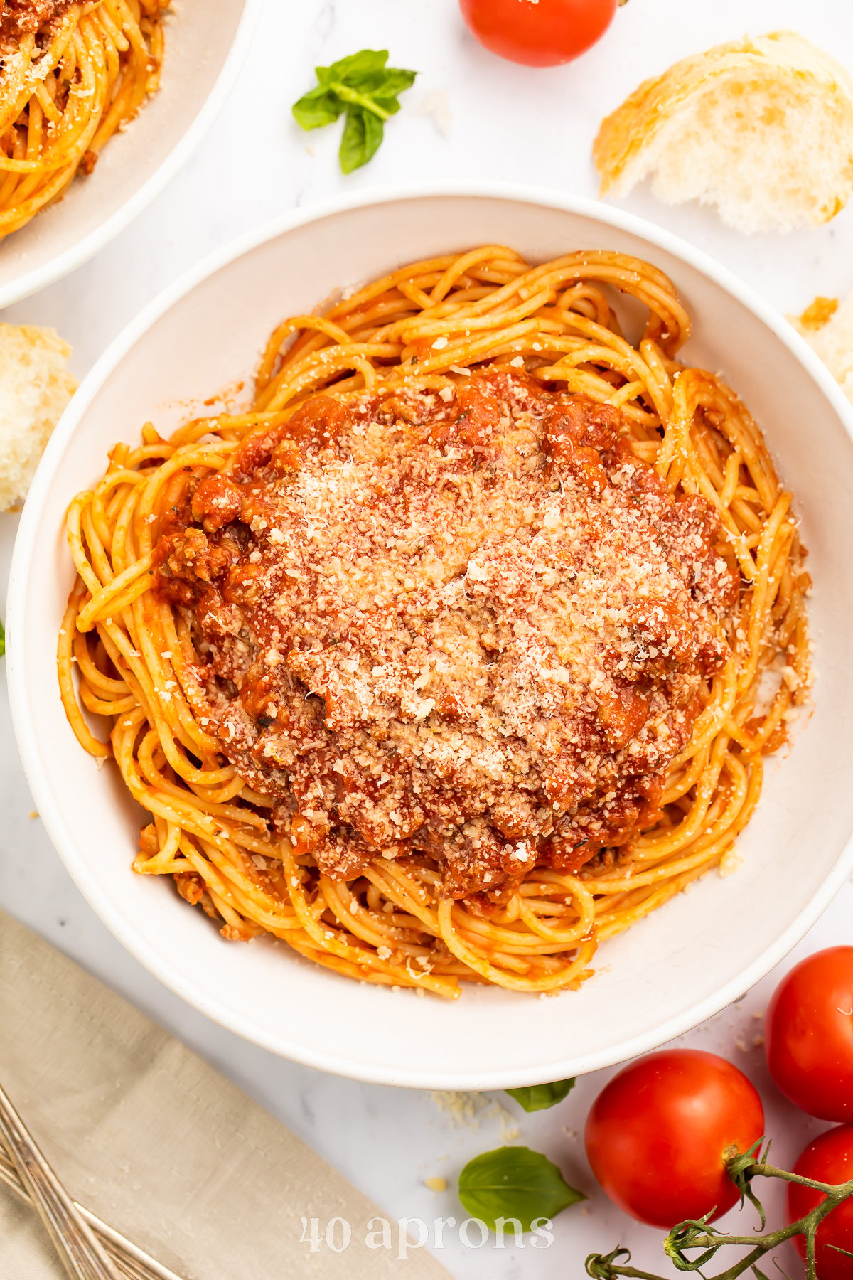 Overhead view of spaghetti noodles coated in rich, red Instant Pot spaghetti sauce in a large white pasta bowl on a table with tomatoes and silverware.