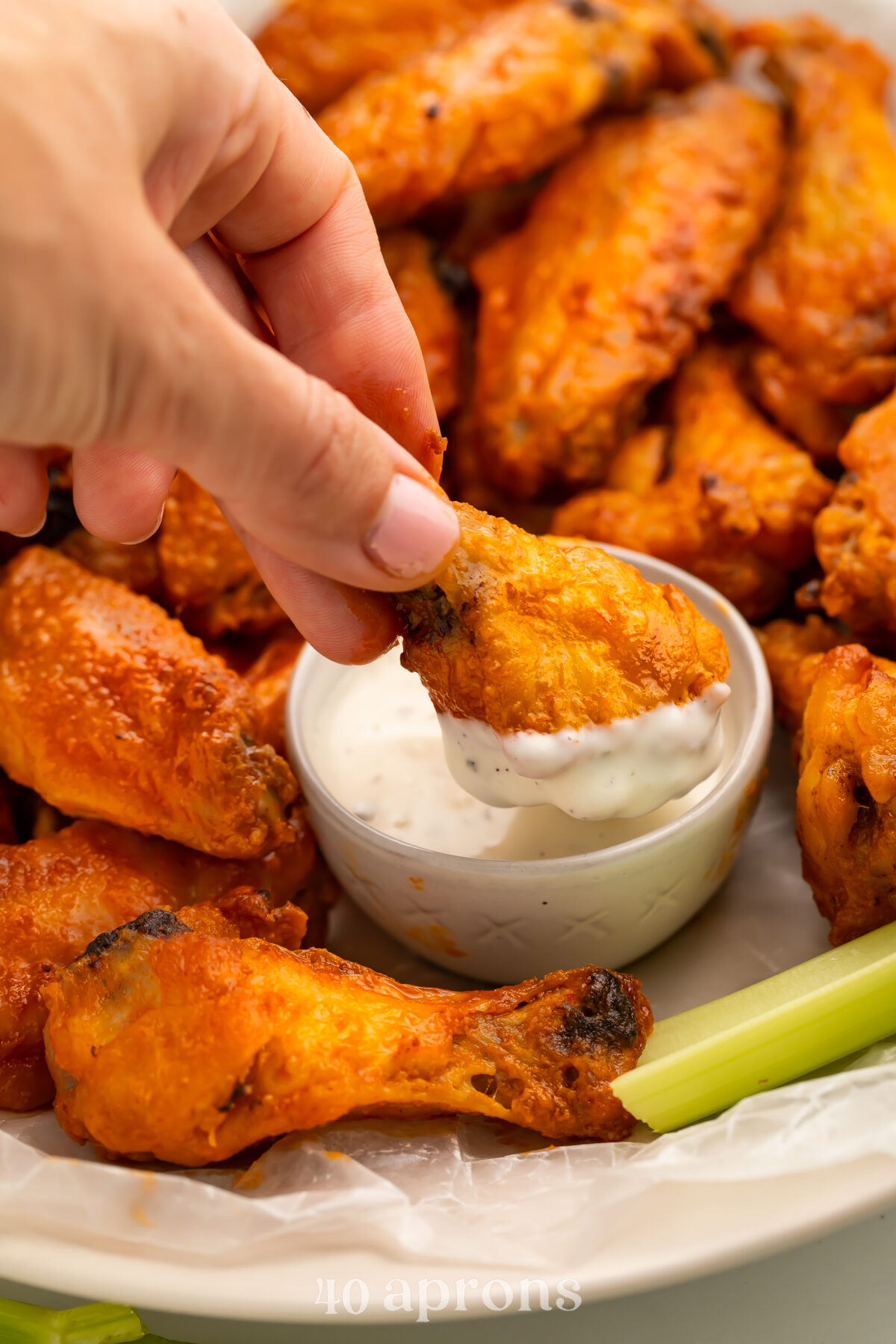 A white hand with painted finger nails, dipping one Whole30 buffalo wing into a small ramekin or Whole30-compatible ranch dressing.