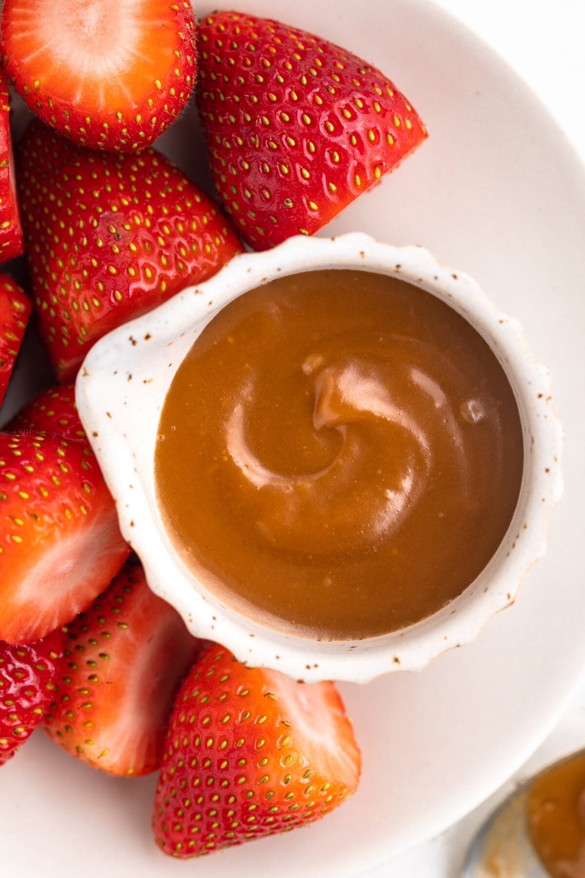 Overhead look at a small ramekin of keto caramel sauce on a plate next to sliced bright red strawberries.