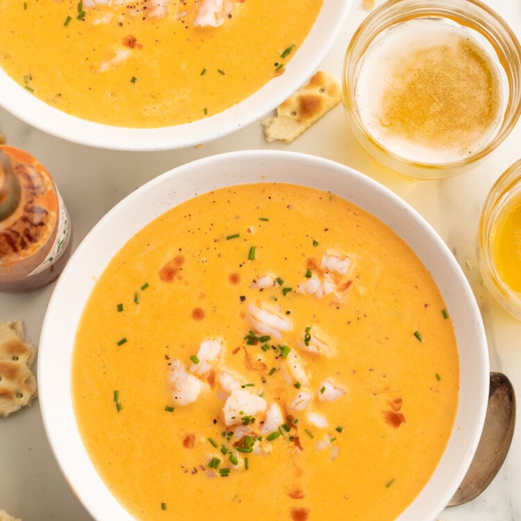 Two bowls of creamy, light orange cajun shrimp bisque, with chunks of shrimp and fresh green herbs in the center of each bowl.
